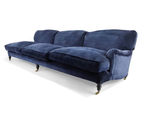 A George Sherlock three seat sofa, in the manner of Howard and Sons, blue velvet upholstery, on turned legs and castors, 82cm