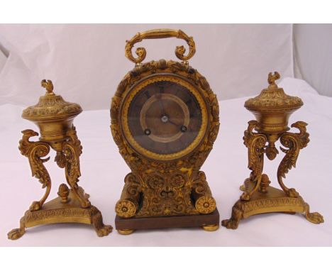A French gilt metal and glass mantle clock with Roman numerals, hinged handle flanked by two urn shaped garnitures on paw fee