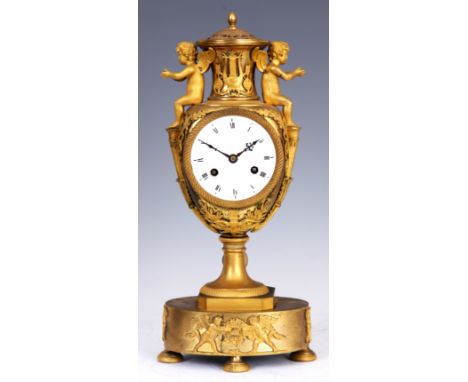 A FINE FRENCH EMPIRE ORMOLU URN-SHAPED MANTEL CLOCK surmounted by two winged cherubs above a 9.5cm enamel dial with Roman num