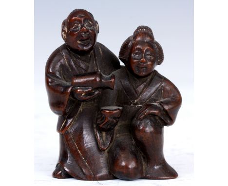A JAPANESE HARDWOOD NETSUKE of a man pouring his wife a drink, signature to his back.
