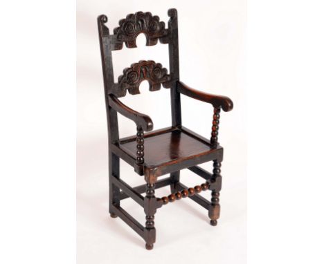 A late 17th century oak Derbyshire chair, the typical shaped ladder back carved with scrolls and masks, associated arms, pane