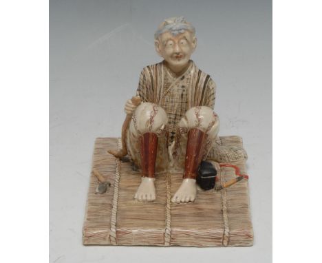 A Japanese Satsuma model, of a seated elder, the tools of his trade at his side, seated on a rush mat, picked out in earth to
