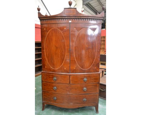 A George III mahogany bow-front linen press, broken architectural pediment crested by an urnular finial and flanked by four f