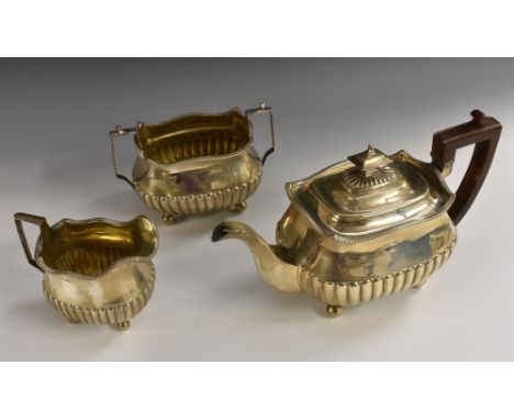 A George III silver three piece half-fluted boat shaped tea service, comprising teapot, milk jug and sugar basin, angular scr