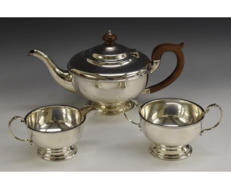 A George V silver three piece tea service, comprising teapot, milk jug and sugar basin, hinged domed cover, scroll capped han