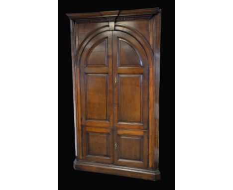 A George III oak floor standing corner cupboard, outswept break-centre cornice above a dentil apron and a pair of arched pane