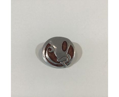 Archibald Knox for Liberty & Co., a silver and enamel brooch, circular, of whiplash design enclosing four shaped sang-de-boeu