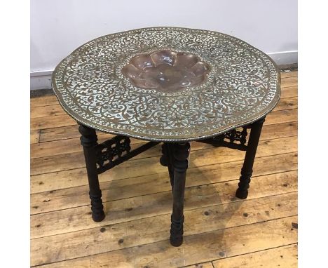 An Indian brass low tray table, Jaipur, early 20th century, the large tray in relief with a dense foliate pattern, on a fret-