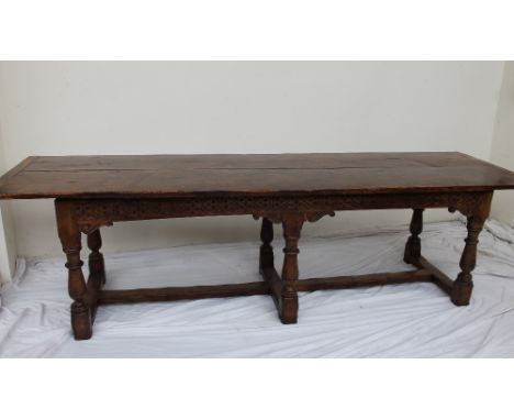 A 17th century style yew refectory table, the planked rectangular top on a carved base with ring turned baluster legs united 