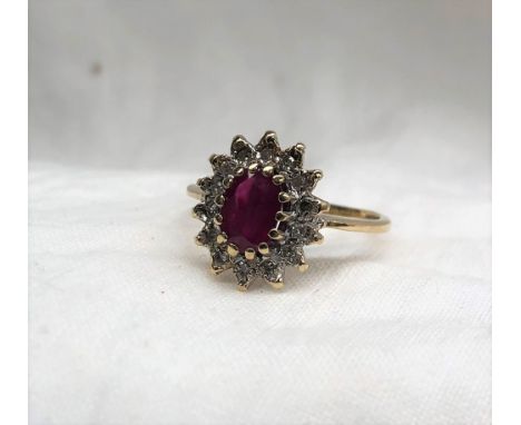 A ruby and diamond cluster ring the central oval faceted ruby surrounded by fourteen diamonds to a white metal setting and 9c