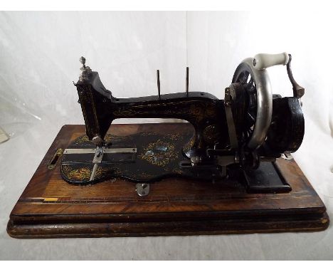 A vintage hand cranked sewing machine, the metal body decorated with mother of pearl inlay contained within a wooden box deco