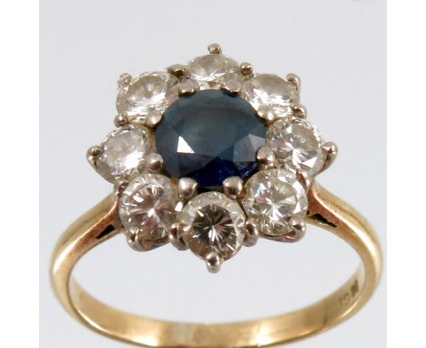 A sapphire and diamond cluster ring, stamped '18ct', the round cut sapphire of approximately 5.5mm diameter, enclosed by eigh