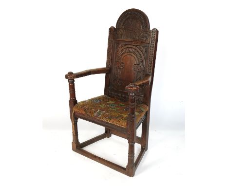 An Antique oak open armchair, with carved solid back, the seat with tapestry upholstery, raised on turned legs united by stre