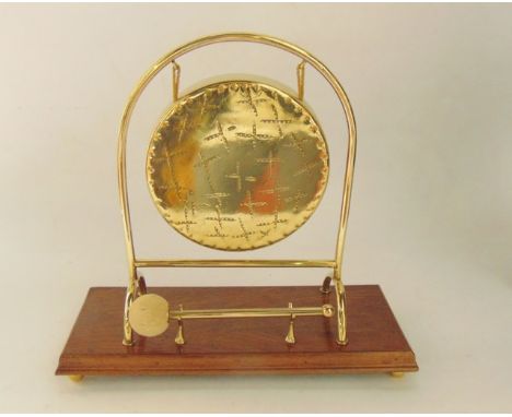 An antique brass dinner gong raised on a U shaped brass bracket, supported on a timber base of rectangular form, raised on fu
