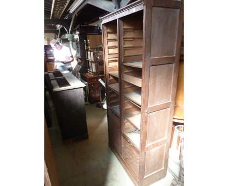 An early 20th century oak freestanding twin office filing cabinet with panelled frame, enclosed by a pair of rise-and-fall ta