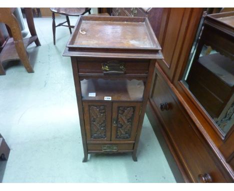 An Edwardian oak floor standing pedestal smokers cabinet partially enclosed by a pair of rectangular panelled doors with carv