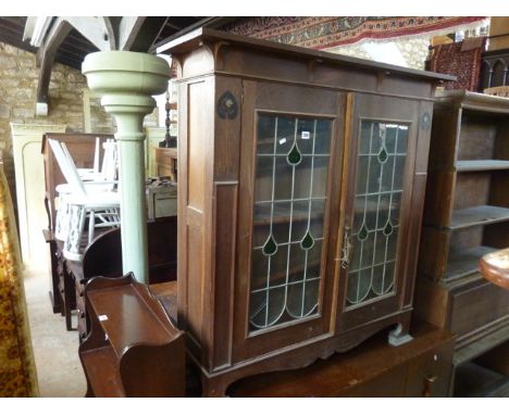 An Edwardian Arts & Crafts style oak side cabinet enclosed by a pair of rectangular leaded light panelled doors with coloured