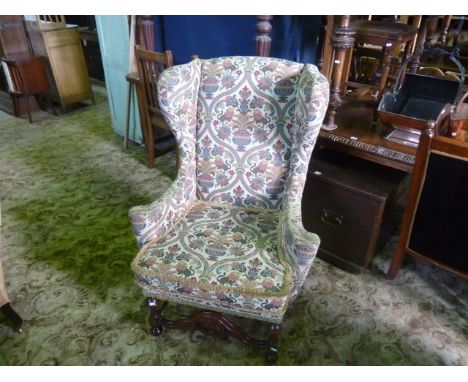 A reproduction wing chair with swept arms, tapestry style upholstery, loose seat cushion and raised on turned forelegs united