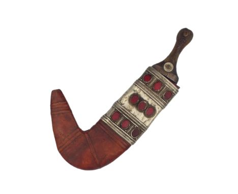A Yemani jambiya dagger, 19th century, with rhino horn handle and leather sheath mounted with white metal and red inset hards
