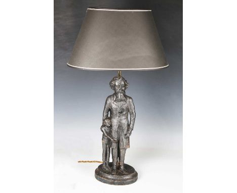 A cast iron table lamp in the form of Charles Dickens and Oliver, fitted with a black shade, height 68cm.