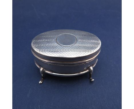 A George V silver oval ring box with engine turned decorated to the hinged lid, raised upon three curved feet.  Birmingham 19