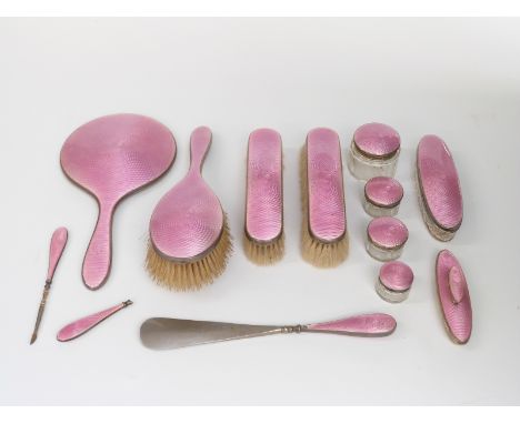 George V pink guilloché enamel dressing table set comprising hand mirror, three brushes, five cut glass pots, miniature tools