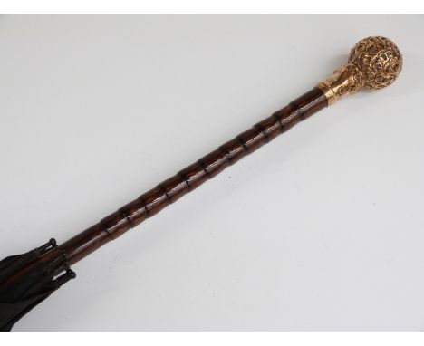 A late 19thC/20thC parasol with spherical yellow metal repoussé decorated handle with cane stick, 85cm