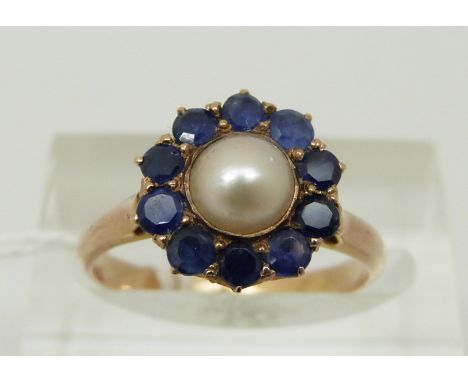 A yellow metal ring set with a pearl to the centre surrounded by sapphires, size L