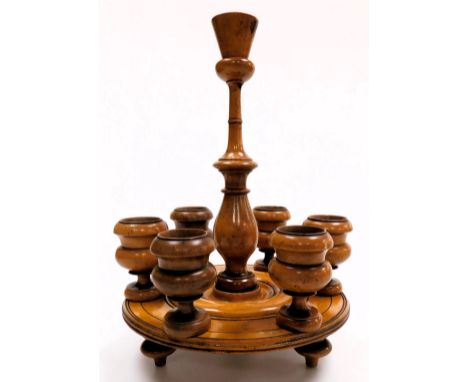 A treen egg stand, with a turned handle, above a circular base, supporting six detachable egg cups, raised on turned feet, 34