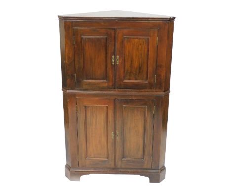 A George III mahogany corner cupboard, the pediment over a pair of panelled doors opening to reveal a fitted shelf, above two
