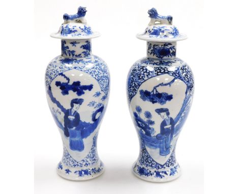 A pair of Qing dynasty blue and white porcelain vases and covers, of baluster form, decorated with reserves of a lady in a ga