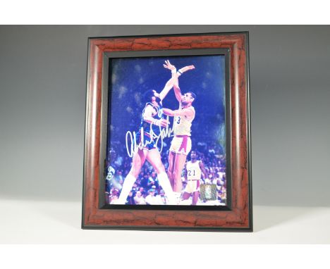 A framed color photograph of Kareem Abdul-Jabbar in action, signed in bold silver ink. The image captures a classic moment be