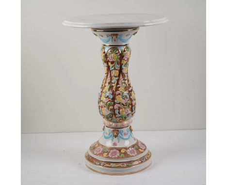 This ornate pedestal table features a richly hand-painted ceramic base in a vibrant palette of pinks, blues, greens, and gold
