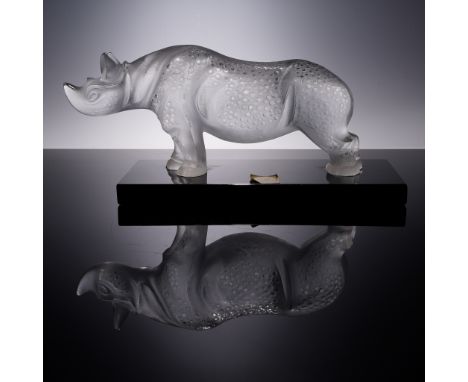 A bold and expressive Lalique crystal figurine featuring a rhinoceros with textured skin and a stylized silhouette, resting o