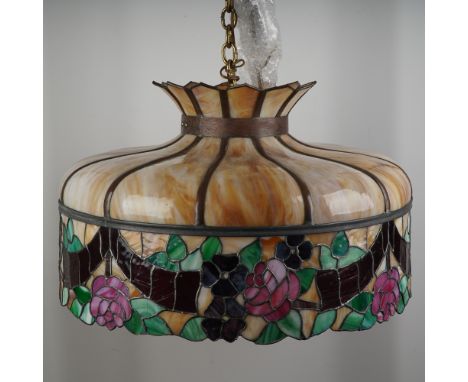 This elegant stained glass pendant lamp features a domed silhouette adorned with swirling caramel-toned panels that transitio