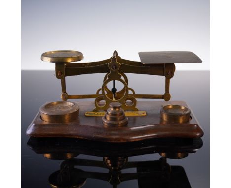 This vintage English balance postal scale features a brass beam mechanism mounted on a polished hardwood base, accompanied by