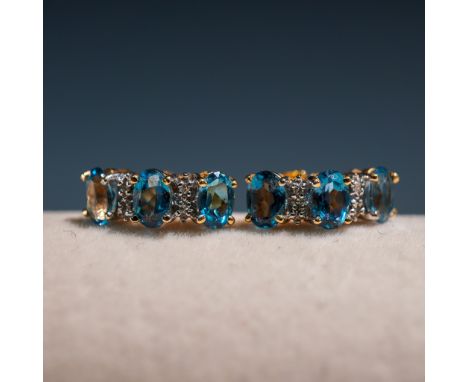 his dazzling pair of 14K gold earrings features oval-cut blue topaz gemstones accented by small round diamonds, creating a vi