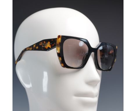 Chic and angular, these Prada cat eye sunglasses feature a bold black front frame paired with warm brown and amber mottled te