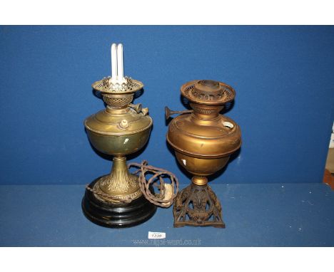 A brass oil lamp on black plinth converted to electric, plus another brass oil lamp (no shade).