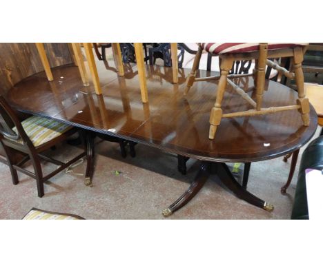 A reproduction mahogany and cross banded D-end dining table with single leaf, set on twin pedestals with tripod bases and bra