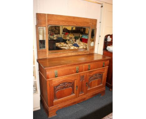 An Arts and Crafts Liberty style carved oak sideboard with two drawers with brass ring and strap handles, scroll carved cupbo
