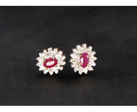 A pair of ruby and diamond earrings, set with a central oval faceted ruby surrounded by two tiers of diamonds to a 9ct yellow