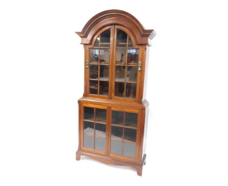 A 20thC mahogany display cabinet, with an arched top, with two glazed panel doors, with glazed panel base and shelves, on bra