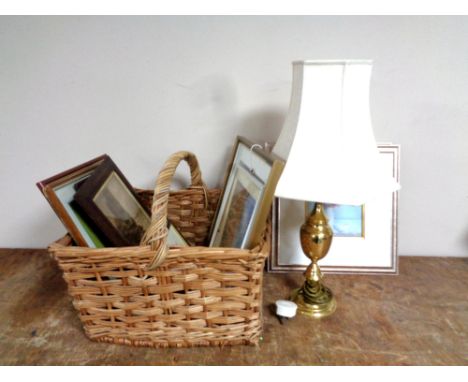A wicker handled basket containing assorted framed pictures and prints, brass table lamp with shade.  