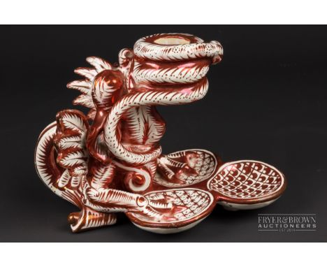 A Cantagalli maiolica candlestick, modelled as a grotesque winged beast holding the sconce in its mouth formed as a coiled sn