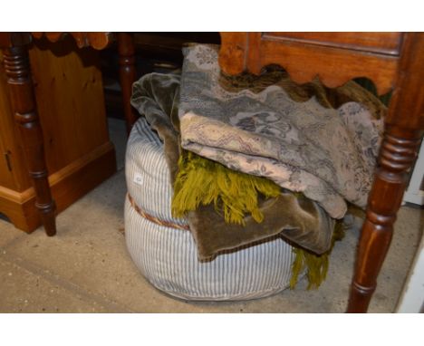 A fabric upholstered pouffe, a floral brocade hanging and a velvet table cover