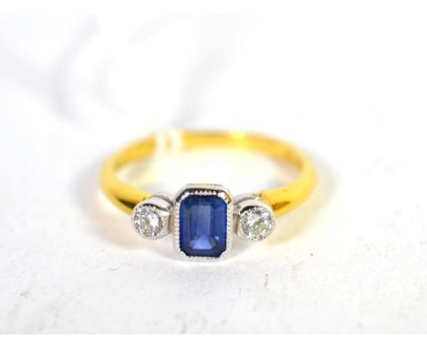 An 18 carat gold sapphire and diamond three stone ring, an emerald cut sapphire spaced by round brilliant cut diamonds in a w