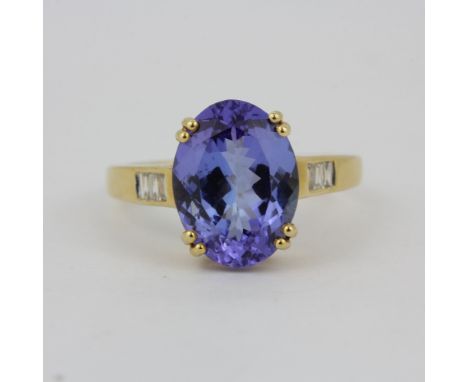 A hallmarked 14ct yellow gold ring set with a large oval cut tanzanite and baguette cut diamond shoulders, stone L. 1.2cm, (O