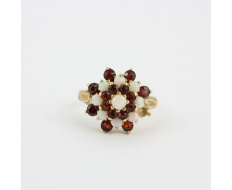 A hallmarked 9ct yellow gold cluster ring set with round cut garnets and opals, (O.5). One garnet missing.