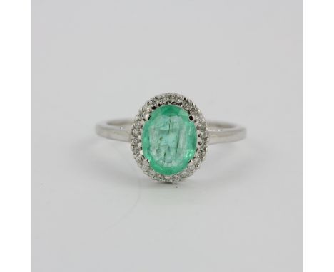 A hallmarked 14ct white gold ring set with an oval cut emerald surrounded by diamonds, (O).